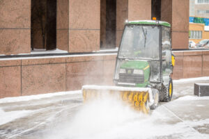 Snow brush clearing a sidewalk in front of an office building